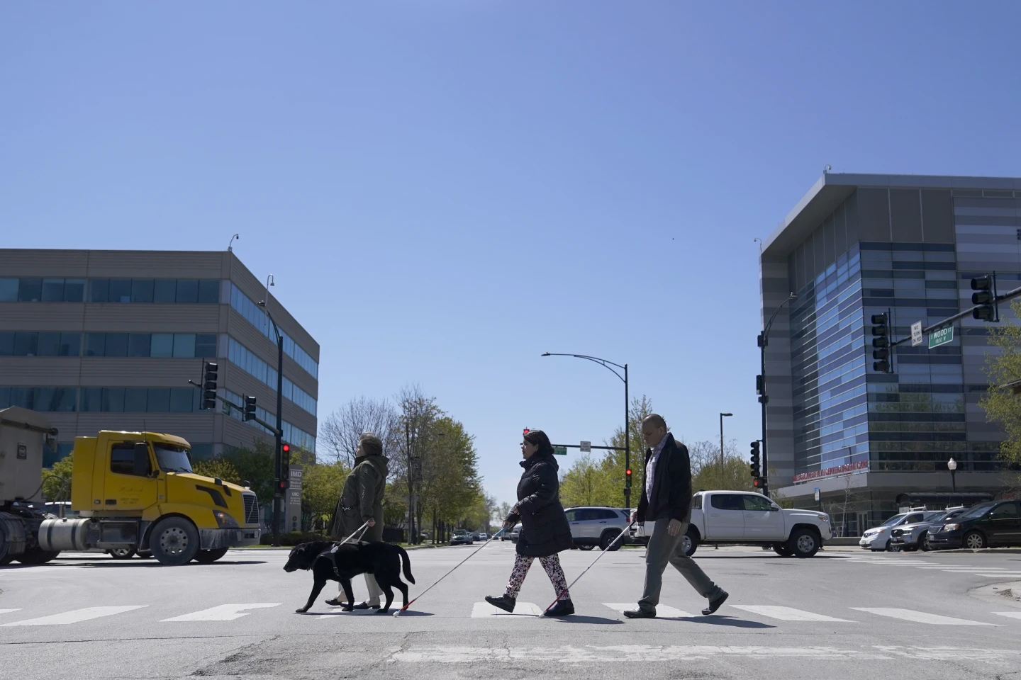 Maureen Reid, left, and her guide dog, Gaston, cross the intersection of Wood Street and Roosevelt Avenue with Sandy Murillo, center, and Geovanni Bahena, relying on an audible signal for the blind, on April 26, 2023, in Chicago.