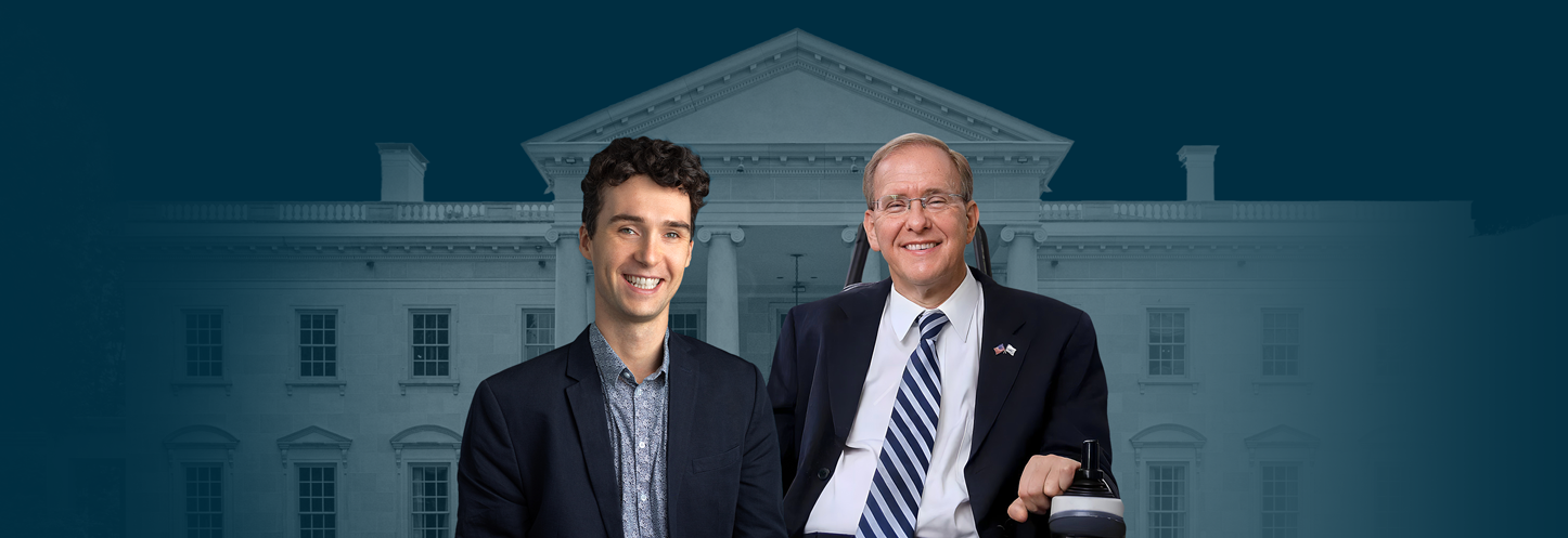 Alt text: "Two men, Congressman Jim Langevin (right) and Charles E. Catherine (left), appear in front of a faded image of the White House. Congressman Langevin, wearing a suit and tie, is seated in a wheelchair and smiling, while Charles E. Catherine, also in formal attire, smiles confidently beside him. The backdrop is a deep blue/green with a subtle view of the White House.