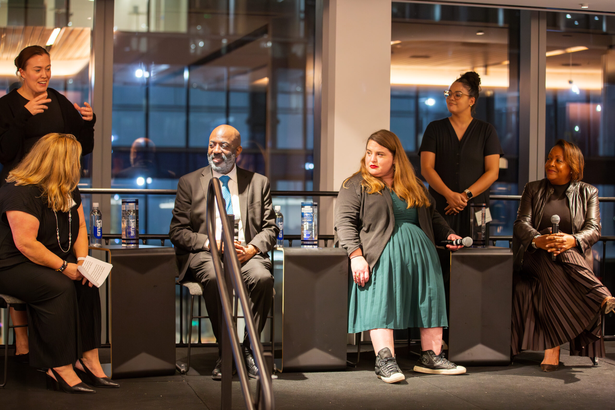 Four panel speakers sit on a stage. On the left side behind them, an ASL interpreter is gesturing. Seated at the stage from right to left, the speakers are: Felicia Nurmsen, Sean Palacio, Maria Town, and Rhonda Nesmith Crichlow.