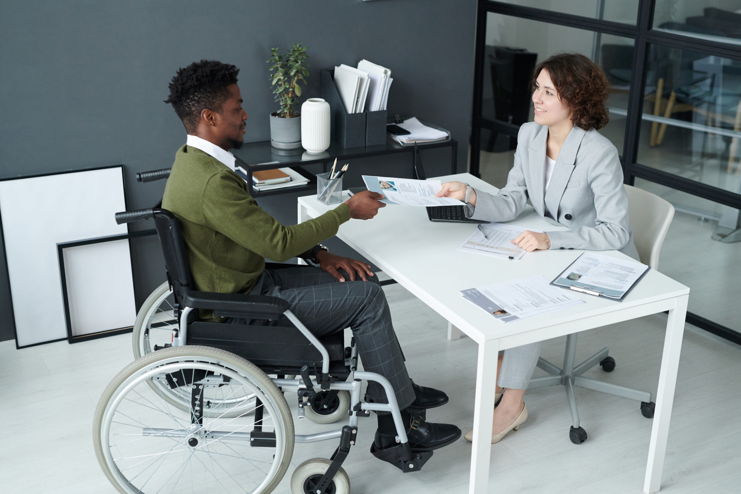 High angle view of businesswoman having job interview with man with disability while they sitting at table in modern office