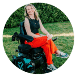 A woman sitting in a power wheelchair with her legs crossed looking directly at the camera smiling