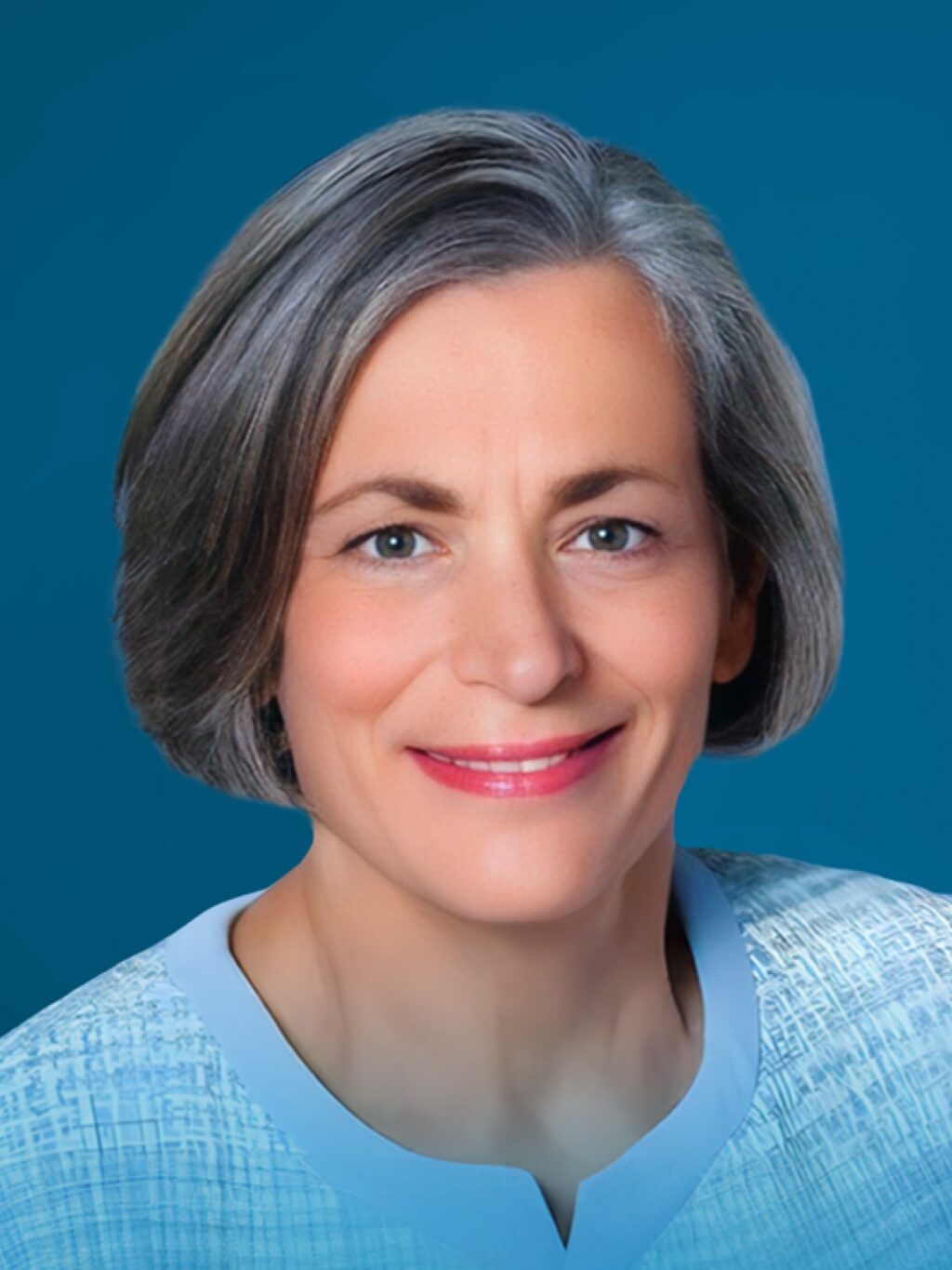 Smiling woman with short gray hair and blue eyes, wearing a light blue blouse with a textured pattern. The background is a solid deep blue. Tone is calm and approachable.