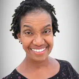 A Black woman with a black shirt and short black hair looks at the camera and smiles big