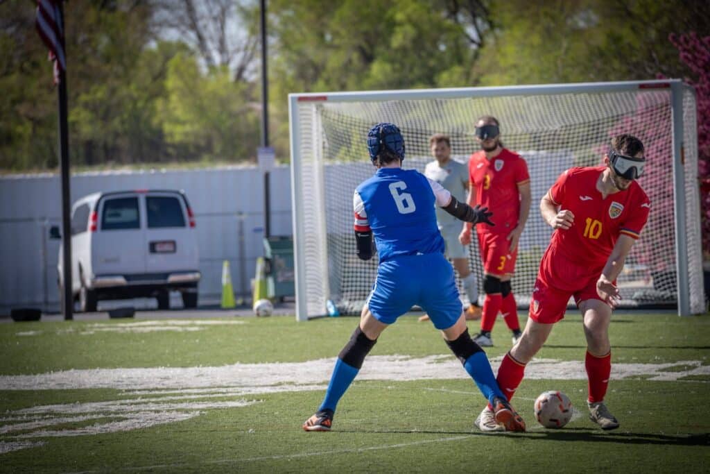A man in a blue uniform intercepting the ball from a man in a red uniform. They wear goggles over their faces