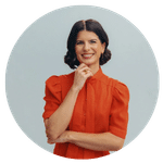 Headshot of Margaux, standing in an orange top and brown hair, with one hand resting on her chin