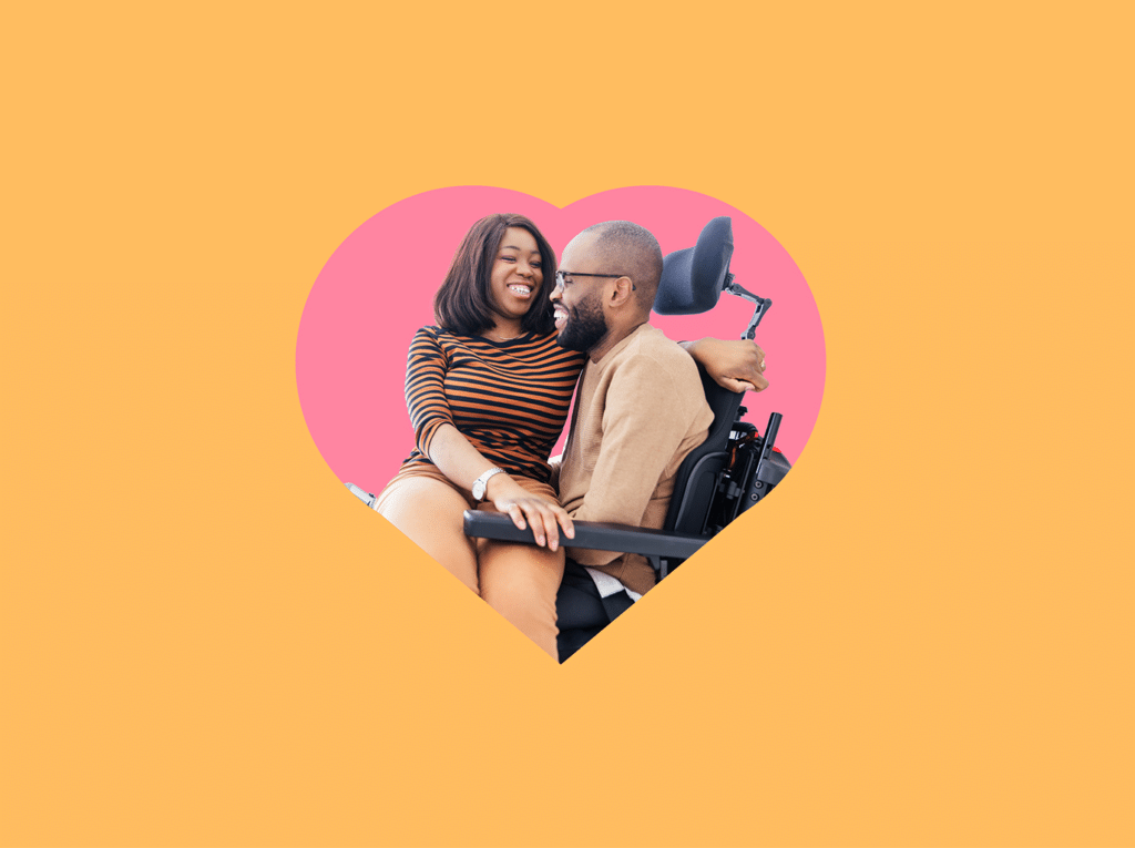 Two adults smiling and sitting close together, one seated in a power wheelchair, framed inside a pink heart shape on an orange background.