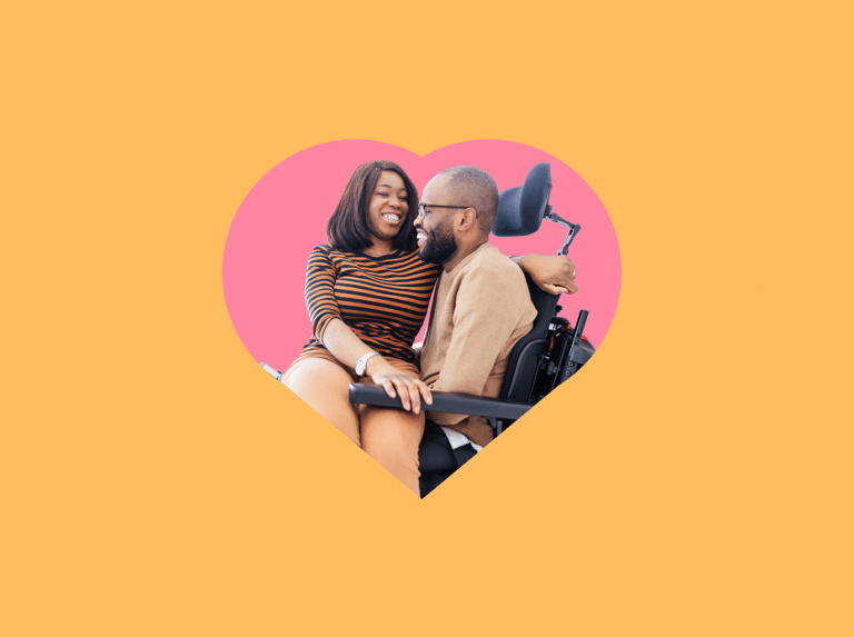Two adults smiling and sitting close together, one seated in a power wheelchair, framed inside a pink heart shape on an orange background.