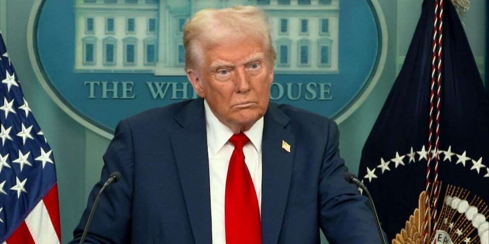 President Donald Trump standing at a podium in the White House briefing room, wide-eyed and seemingly unhappy.