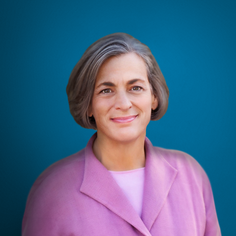 Beth Sirull smiling, wearing a pink jacket in front of a blue background.