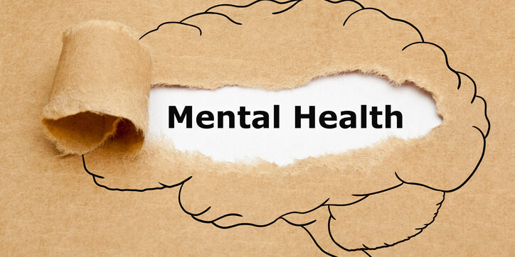 Text Mental Health appearing behind torn brown paper with drawn human brain on it.