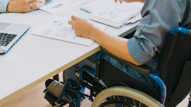 Person in wheelchair reviewing business charts and graphs at desk with laptop