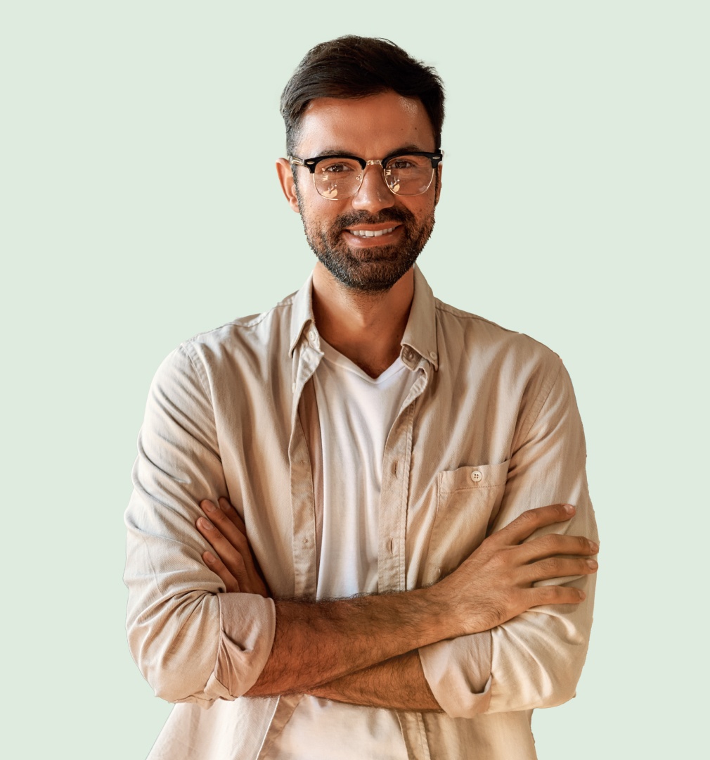 Smiling man with glasses and beard wearing beige button-up shirt with arms crossed