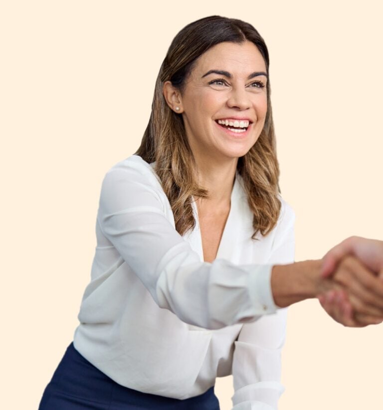 Smiling woman with brown hair, wearing a white blouse, shakes hands confidently. She exudes positivity against a light beige background.