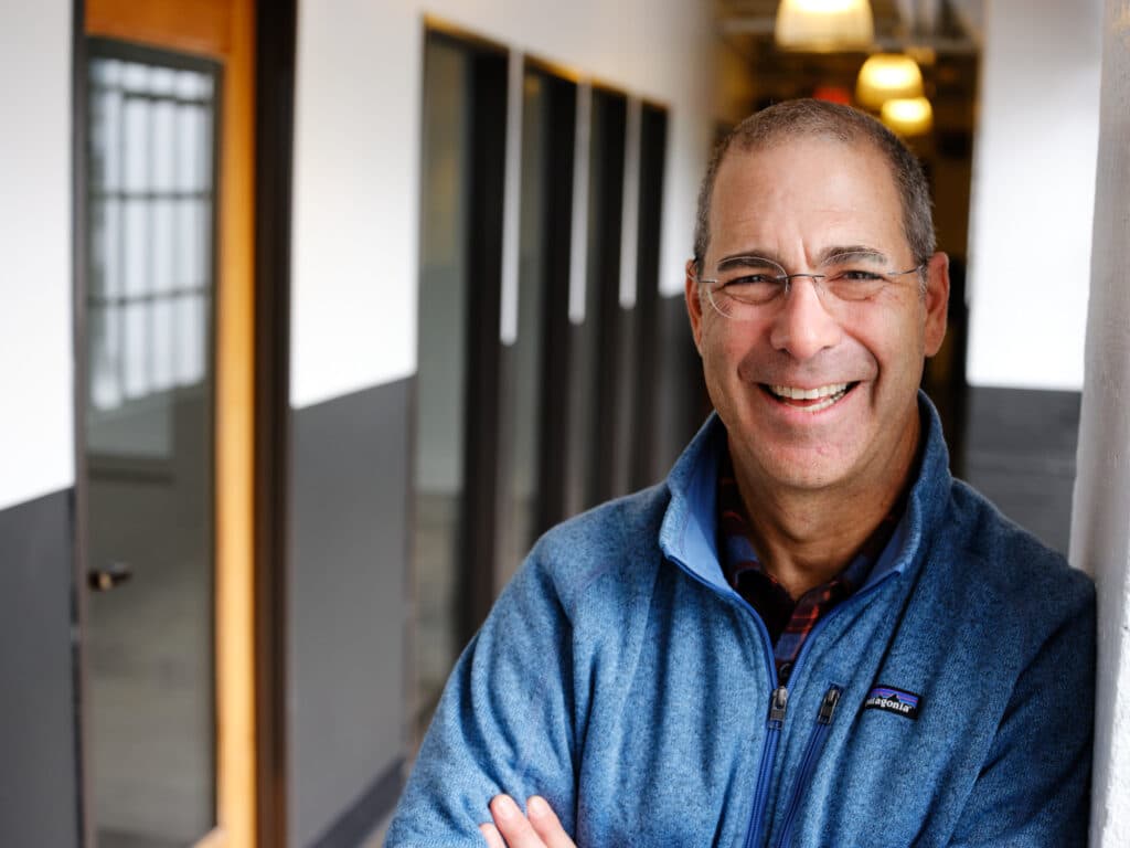 A man wearing a blue shirt and glasses smiling brightly at the camera