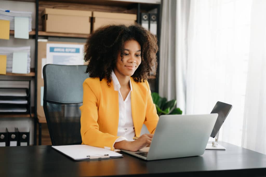Businesswoman working at a desk in a modern office with a notepad and open laptop