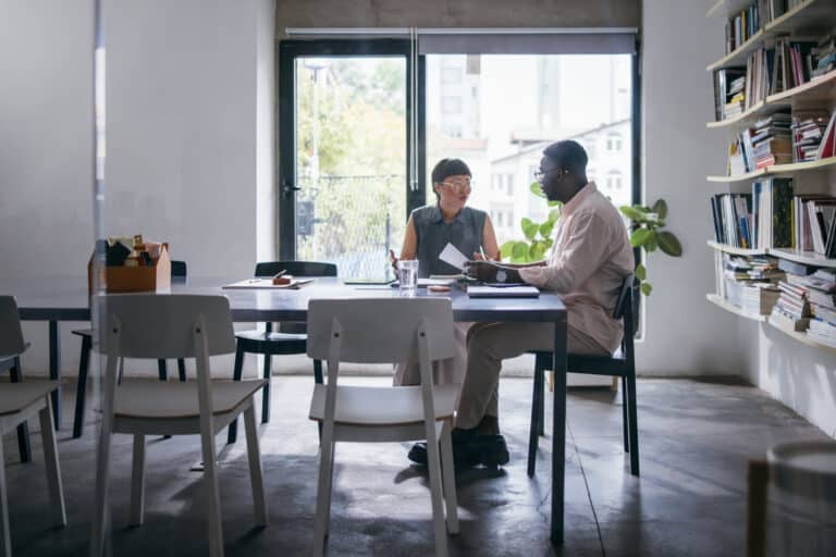 A Japanese woman and African-American man talking about a business project while sitting at the desk.