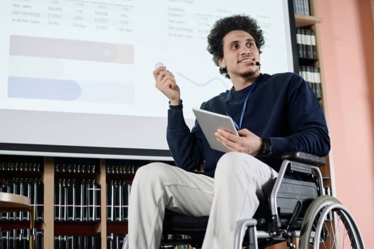 Low angle view of self-confident Middle Eastern student with disability holding digital tablet doing presentation at event in college library
