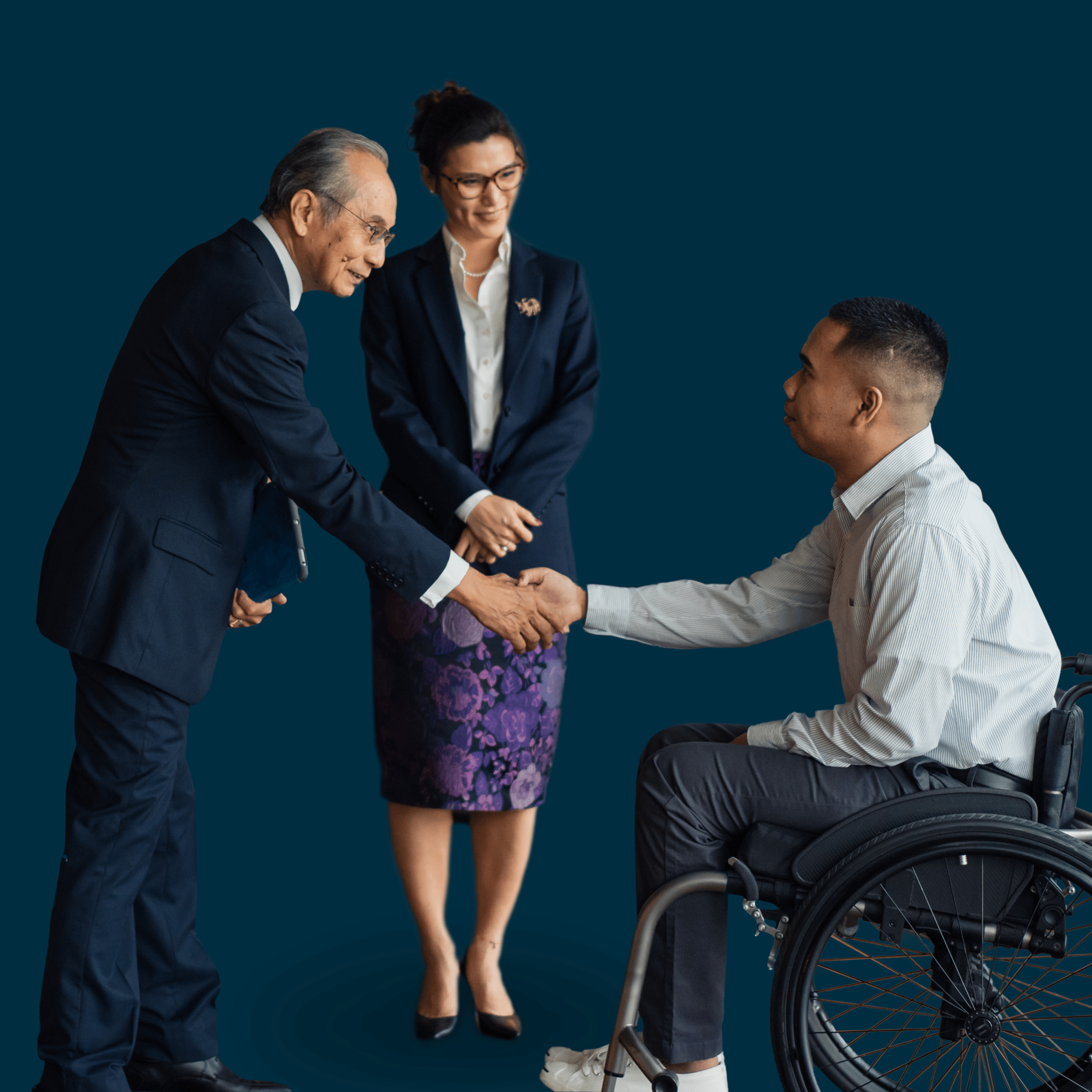 Three business professionals greet one another, including a man using a wheelchair shaking hands with another man while a woman stands nearby.