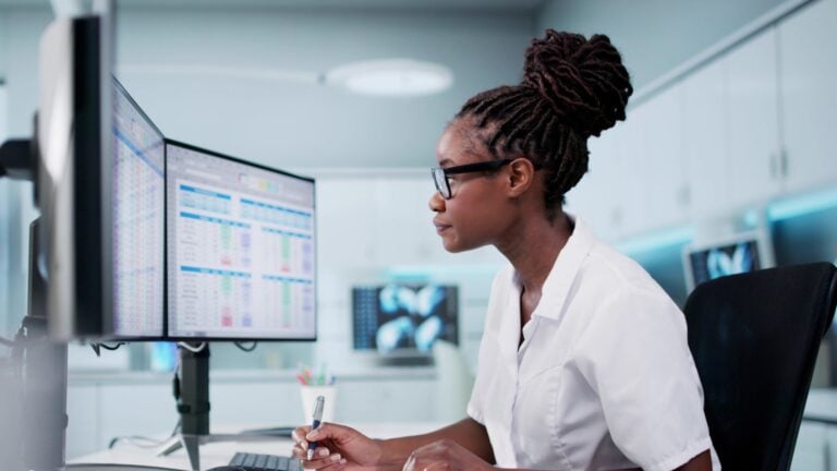 Woman on the computer with a white shirt writing down on a paper