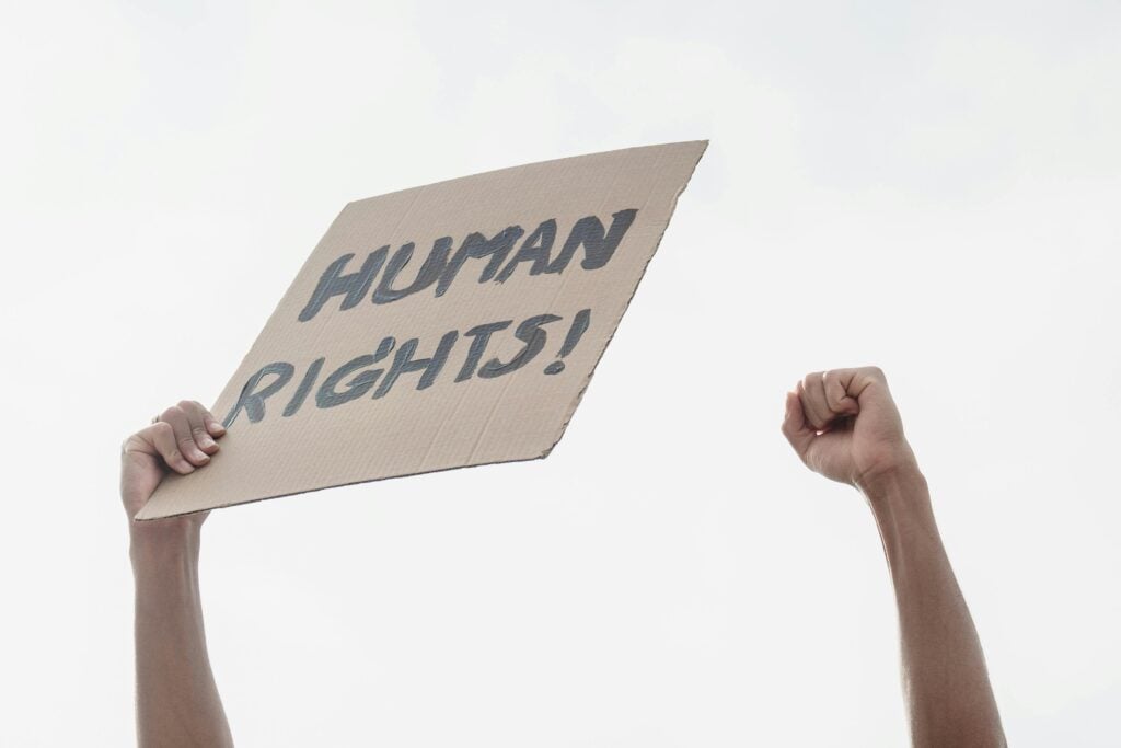 Outstretched hands holding a paper sign that reads "Human Rights!"