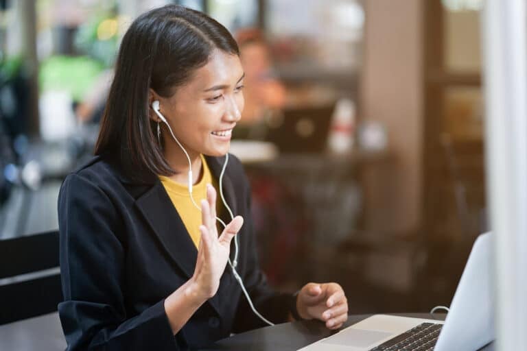 A woman wearing headphones waving to her laptop screen