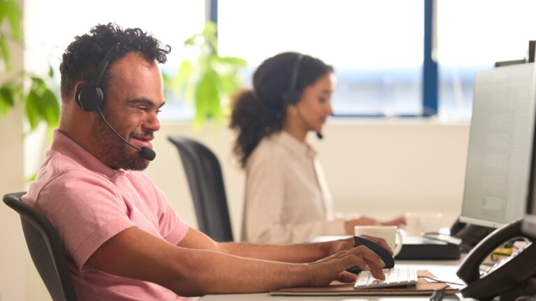Individual on the computer smiling, with another person in the background slightly blurred